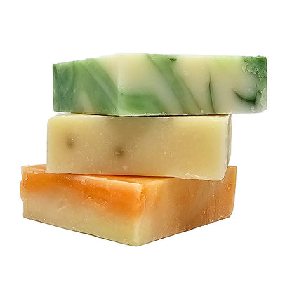 Three bars of shea butter soap in different colors stacked on a white background