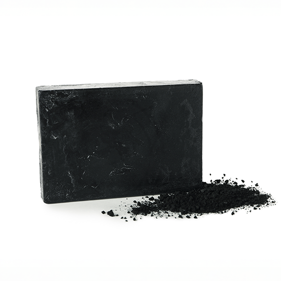 Block of black activated charcoal soap with a small charcoal pile on a white background