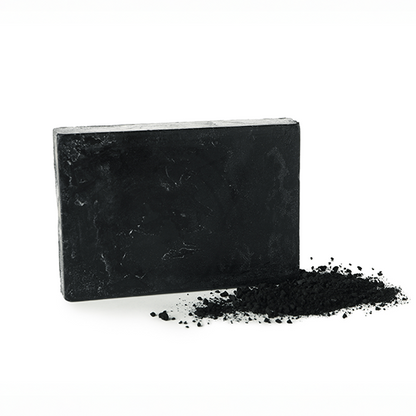Block of black activated charcoal soap with a small charcoal pile on a white background