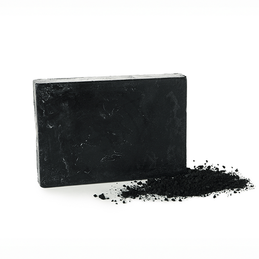Block of black activated charcoal soap with a small charcoal pile on a white background